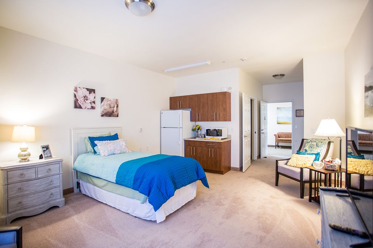 A modern bedroom with a single bed and kitchenette, featuring bright decor.