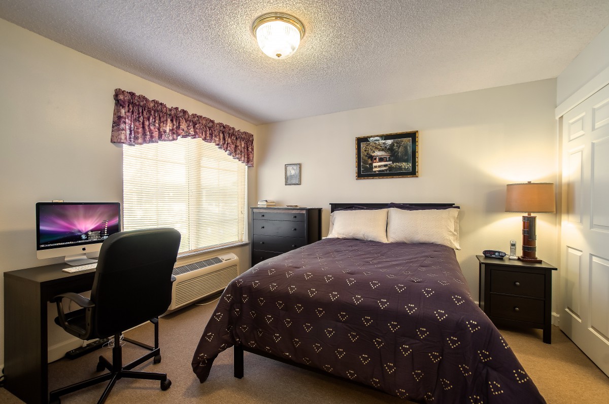 A cozy bedroom with a bed, desk, chair, and window adorned with curtains.
