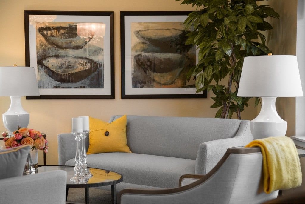 A modern living room with a gray sofa, yellow accent pillow, framed artwork, and decorative elements.