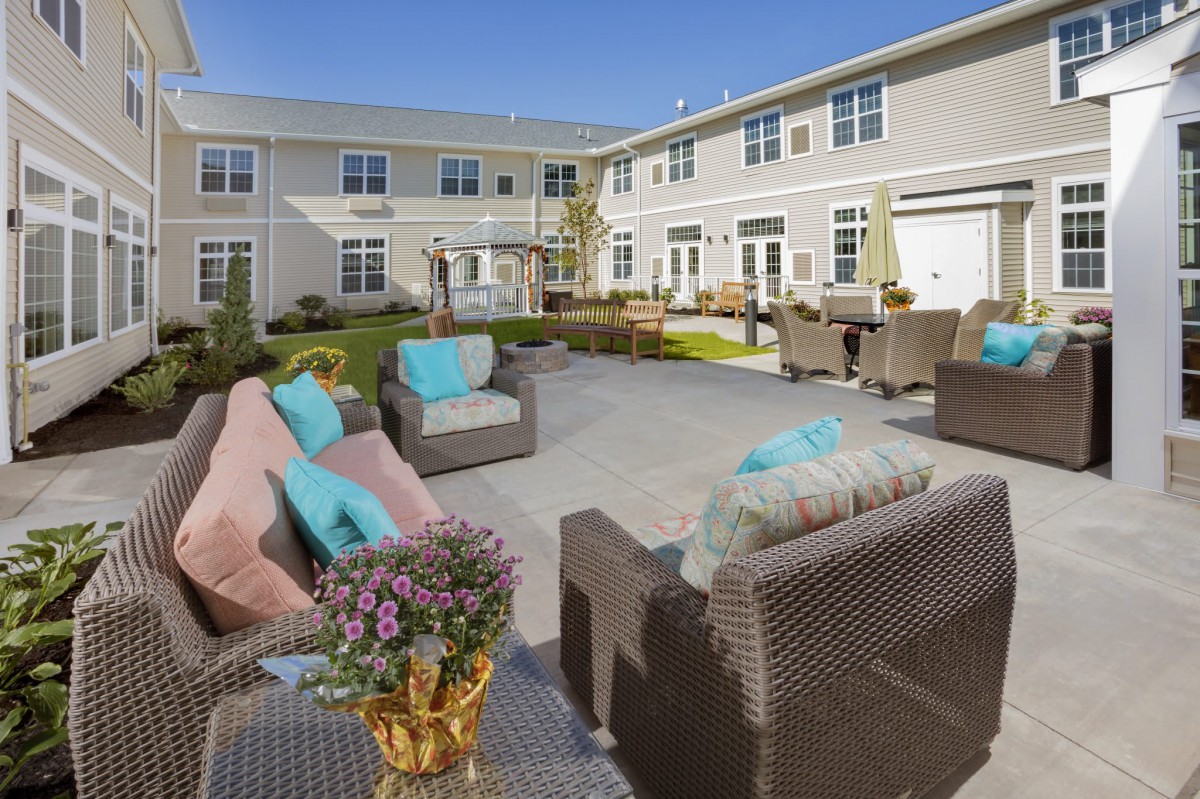 A spacious outdoor patio with comfortable seating and vibrant cushions, set in front of a modern apartment building.