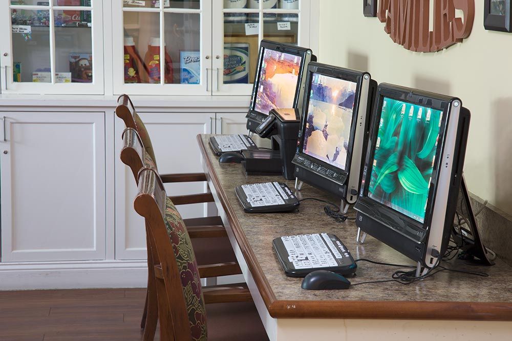 A row of computers with monitors, keyboards, and mice set up on a wooden table in an office.