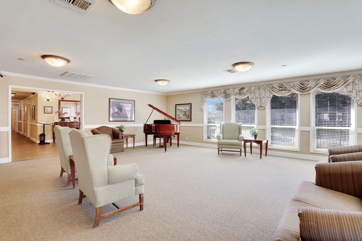 A spacious living room with a piano, several chairs, and large windows.