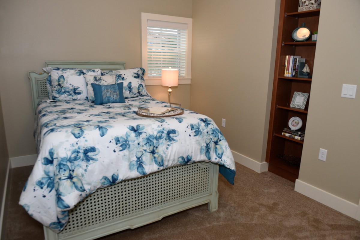 A cozy bedroom with a floral comforter, soft lighting from a bedside lamp, and a bookshelf filled with decor.