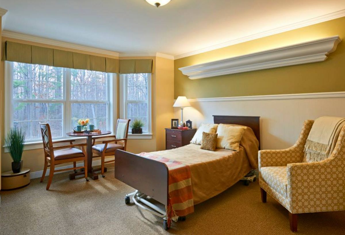 A cozy bedroom with a single bed, armchair, and a table by the window.