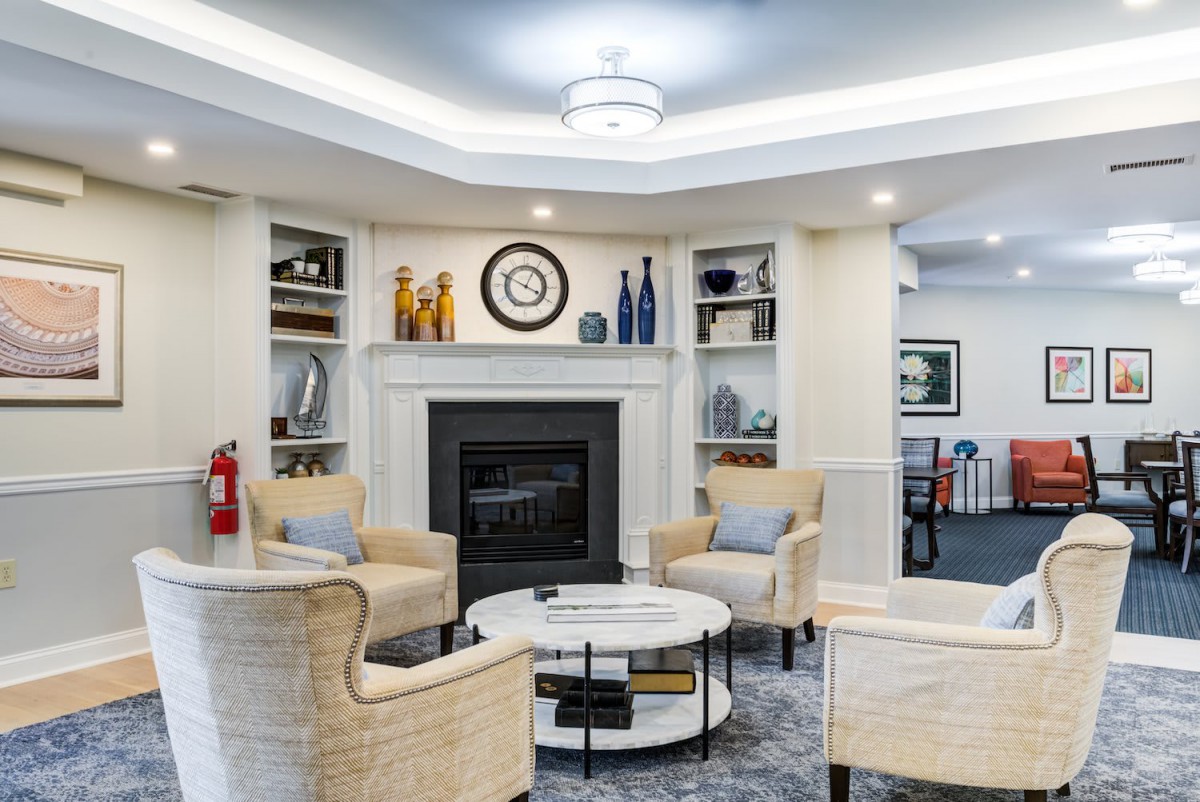 A cozy living room with a fireplace, surrounded by comfortable chairs and decorative shelves.