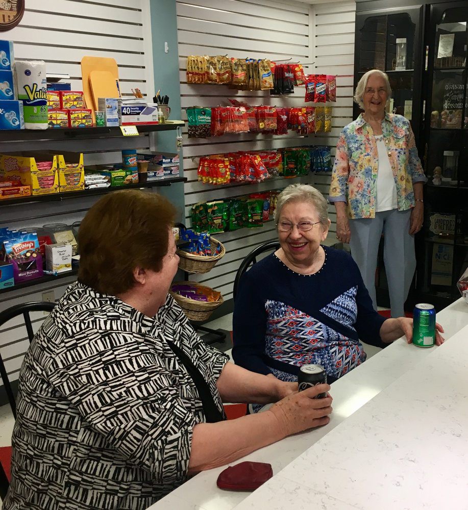 A group of people sitting and chatting in a store with shelves stocked with various products.