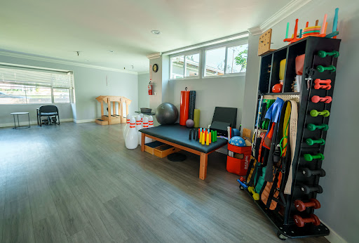 A well-lit therapy space designed for exercise and fitness activities, featuring colorful equipment and a spacious layout.