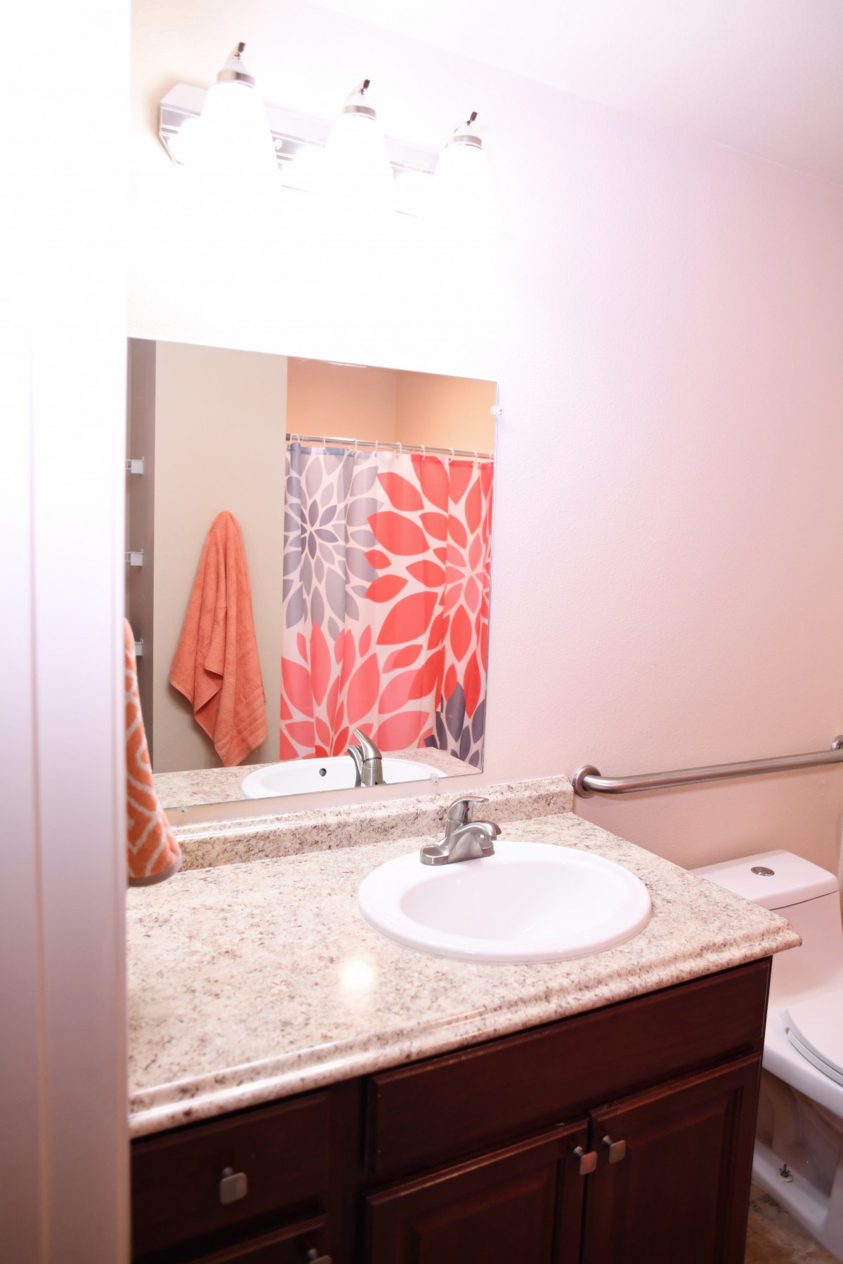 A bathroom with a mirror above the sink, featuring a floral shower curtain and an orange towel.