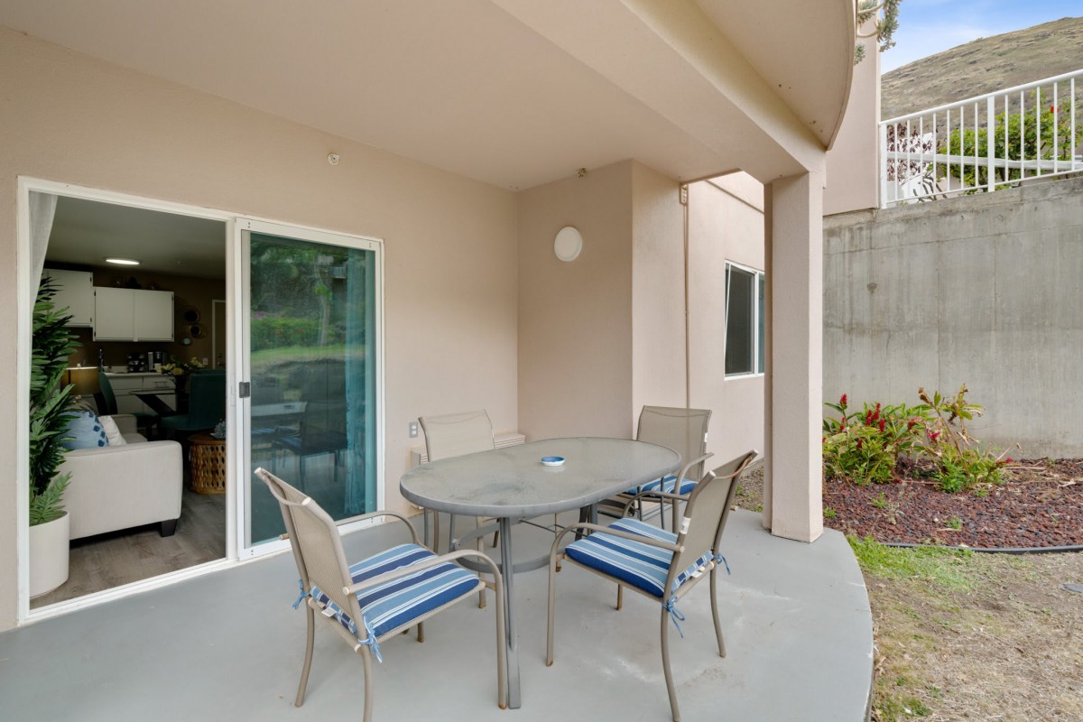 A cozy patio area with a round table and four chairs, positioned near a sliding glass door, under a covered roof.