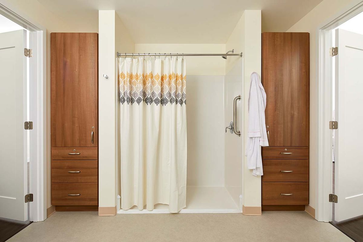 A bathroom with a shower curtain, wooden cabinets, and a hanging white robe.