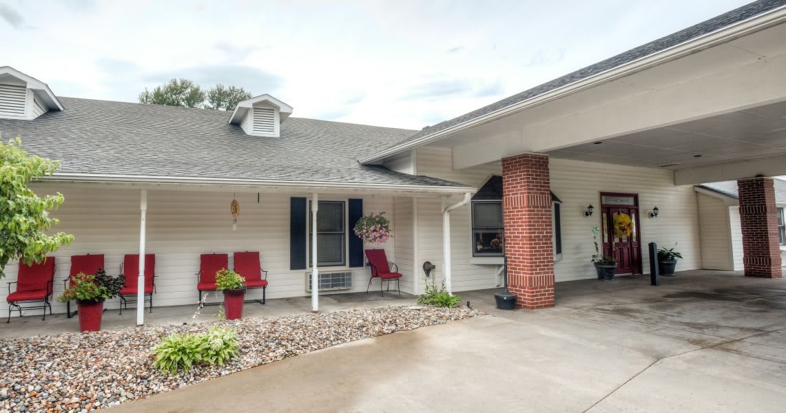 A cozy house with a front porch featuring red chairs, a garage, and a driveway.