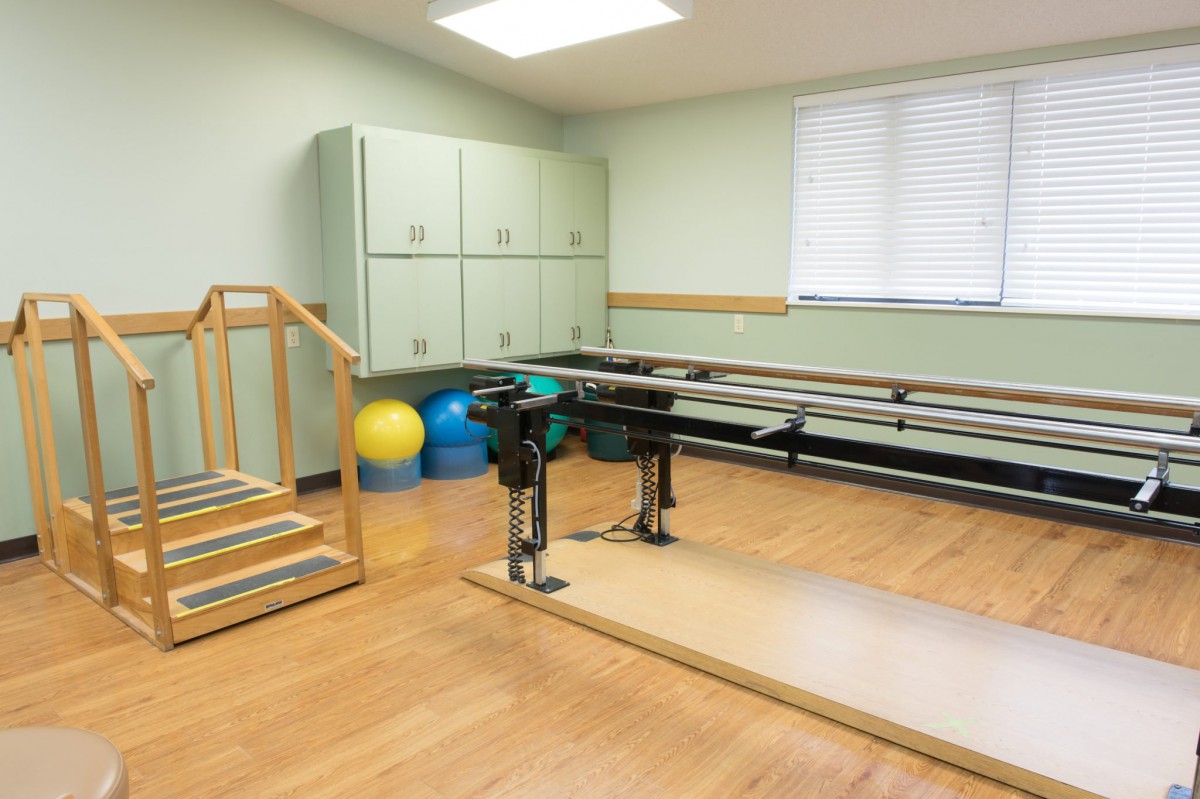 A physical therapy room equipped with balance bars, stairs, and fitness balls for rehabilitation exercises.