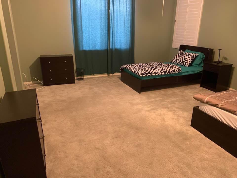 A spacious bedroom with a single bed, dresser, and carpeted floor.