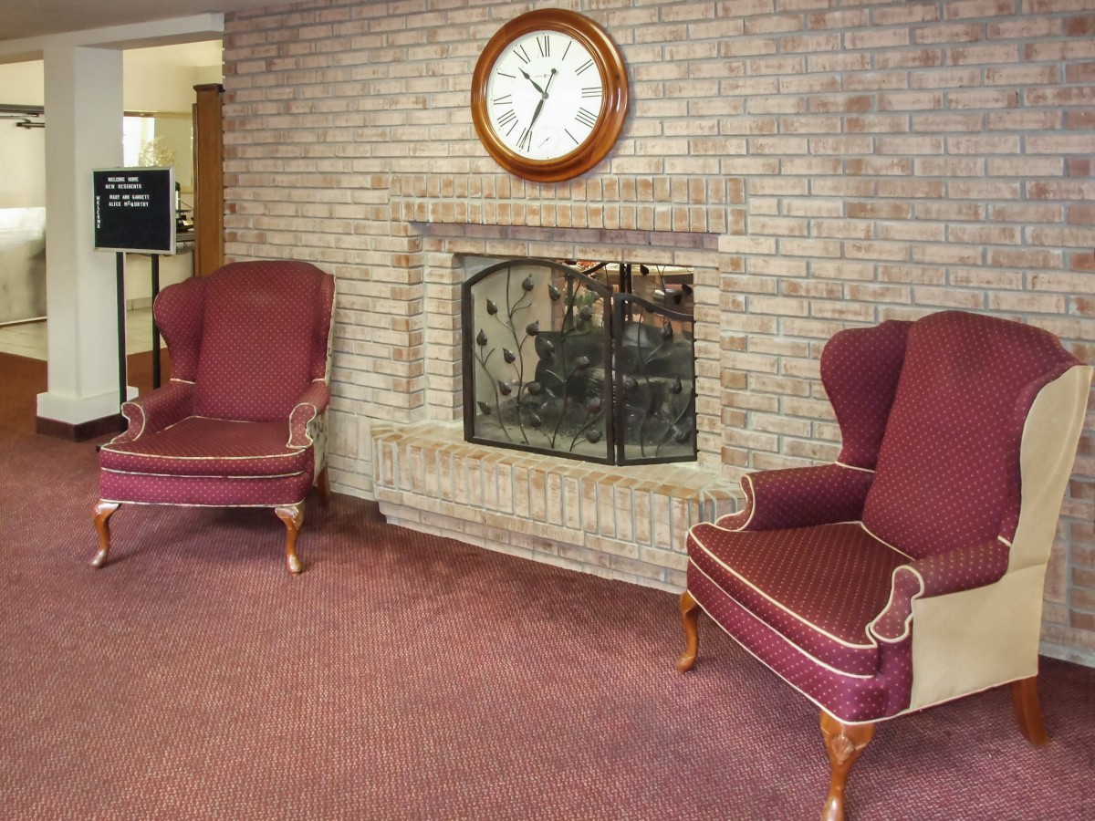 A cozy seating area with a brick fireplace, two armchairs, and a clock on the wall.