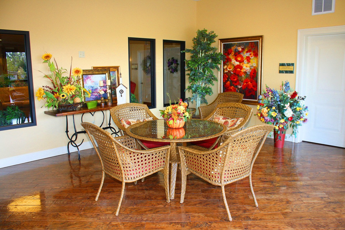 A cozy dining area with wicker furniture, surrounded by vibrant floral arrangements and artwork.