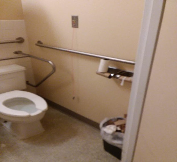 An accessible bathroom with handrails, a toilet, and a trash can.
