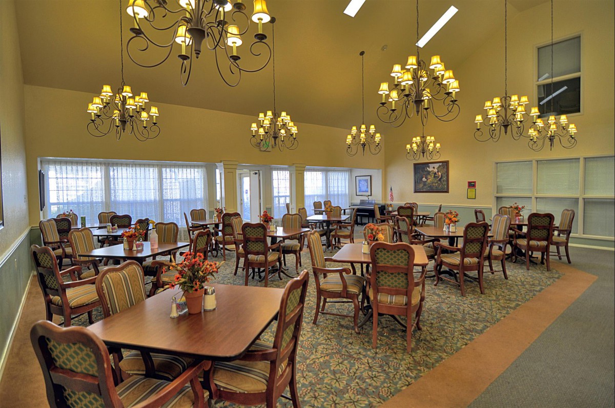 A spacious dining room with elegant chandeliers and neatly arranged tables and chairs.