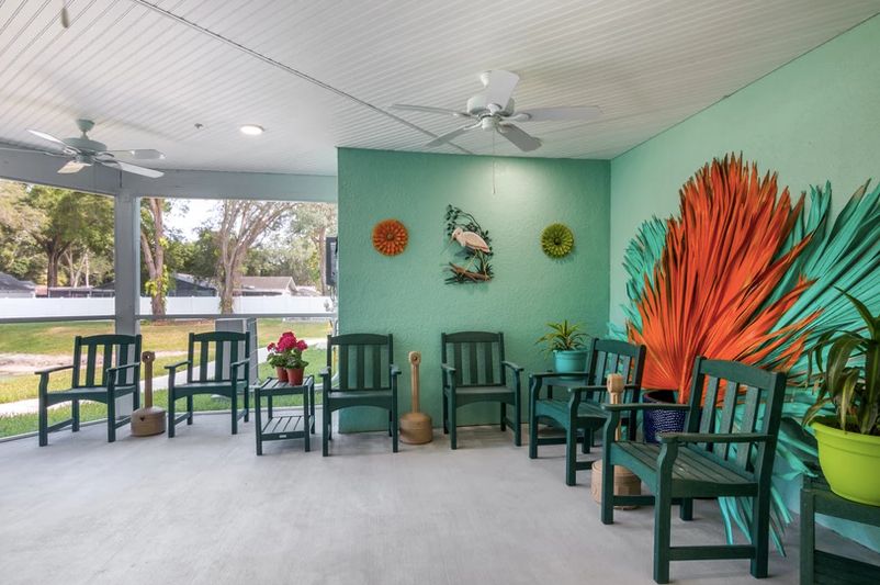 A brightly decorated outdoor seating area with colorful wall art and green chairs.
