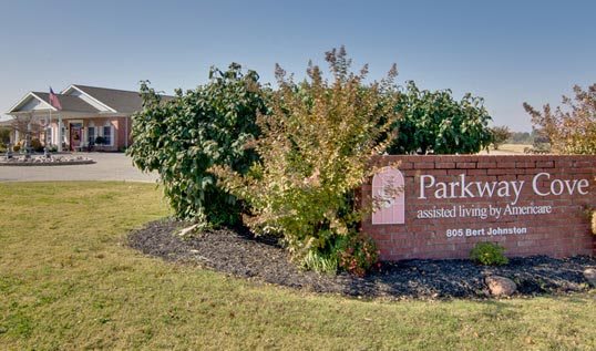 A landscaped area with bushes and a brick sign displaying text.