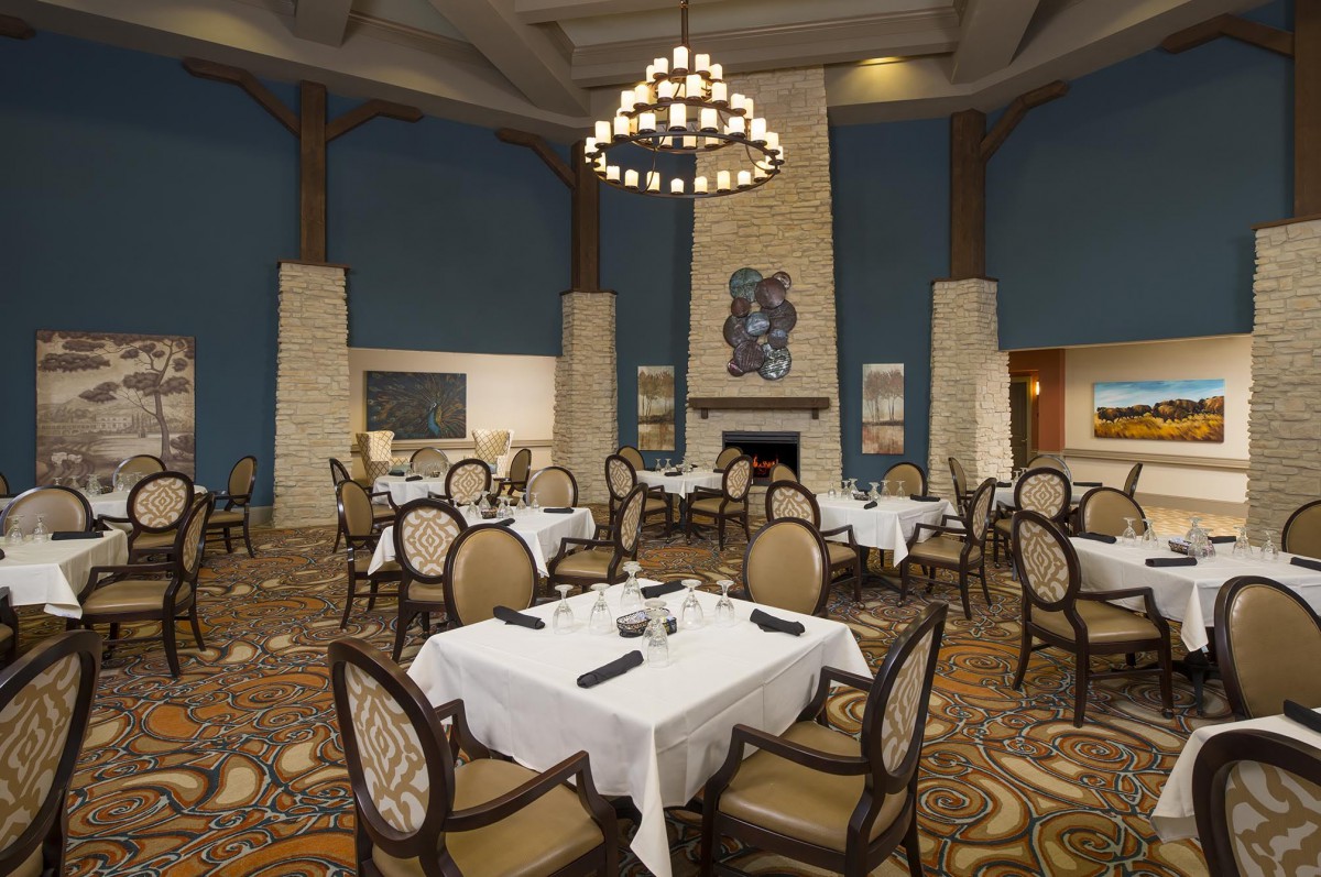 An elegant restaurant interior featuring neatly arranged dining tables, classic chairs, a central chandelier, and a cozy fireplace.