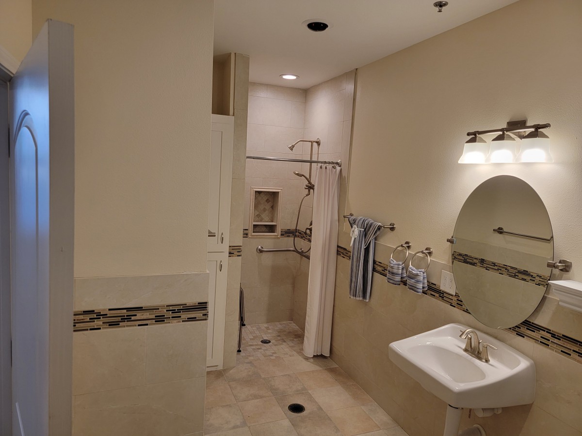 A spacious bathroom featuring a walk-in shower, sink with a mirror, and neatly arranged towels.
