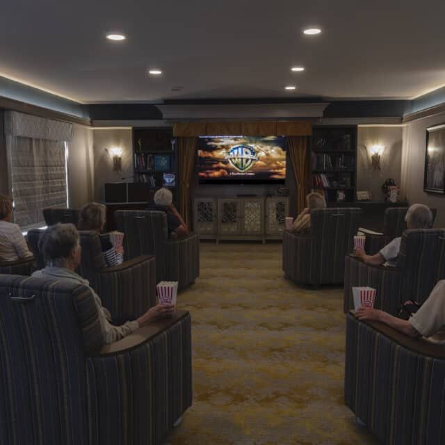 A cozy home theater room with people seated and watching a movie on the screen.