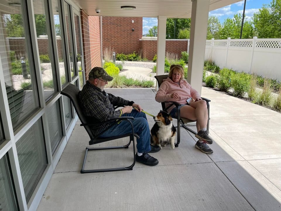 Two people sitting on a patio with a dog between them.