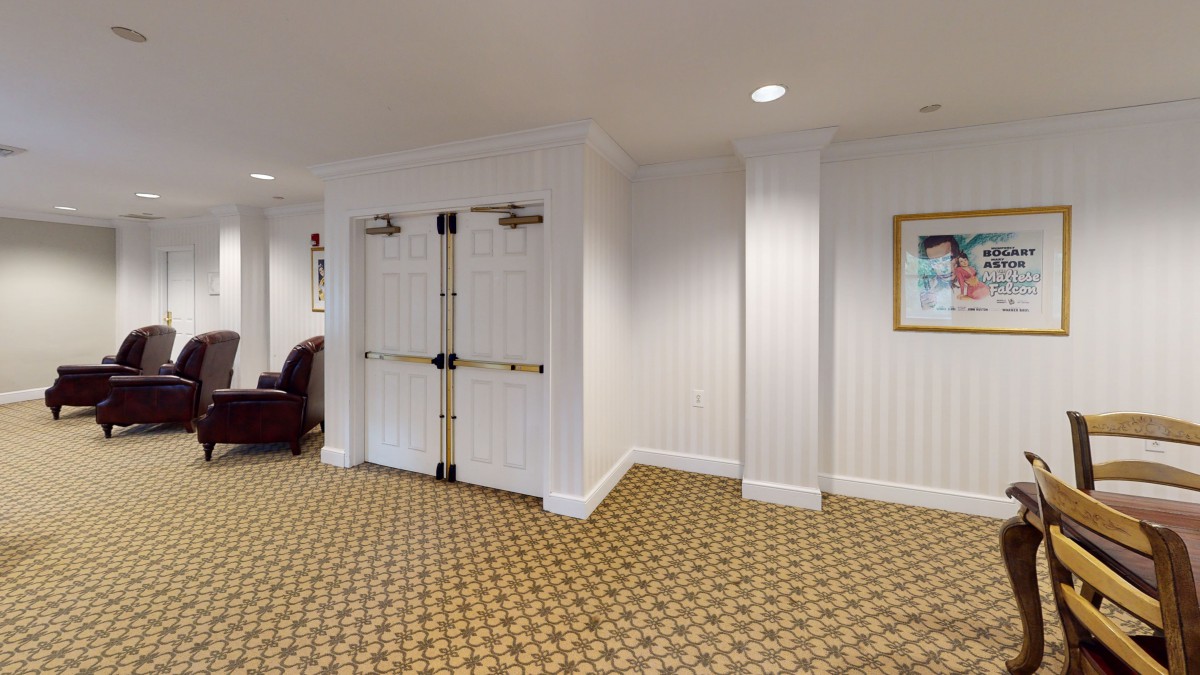 A well-lit hallway featuring double doors, patterned carpet, and framed artwork on the wall.