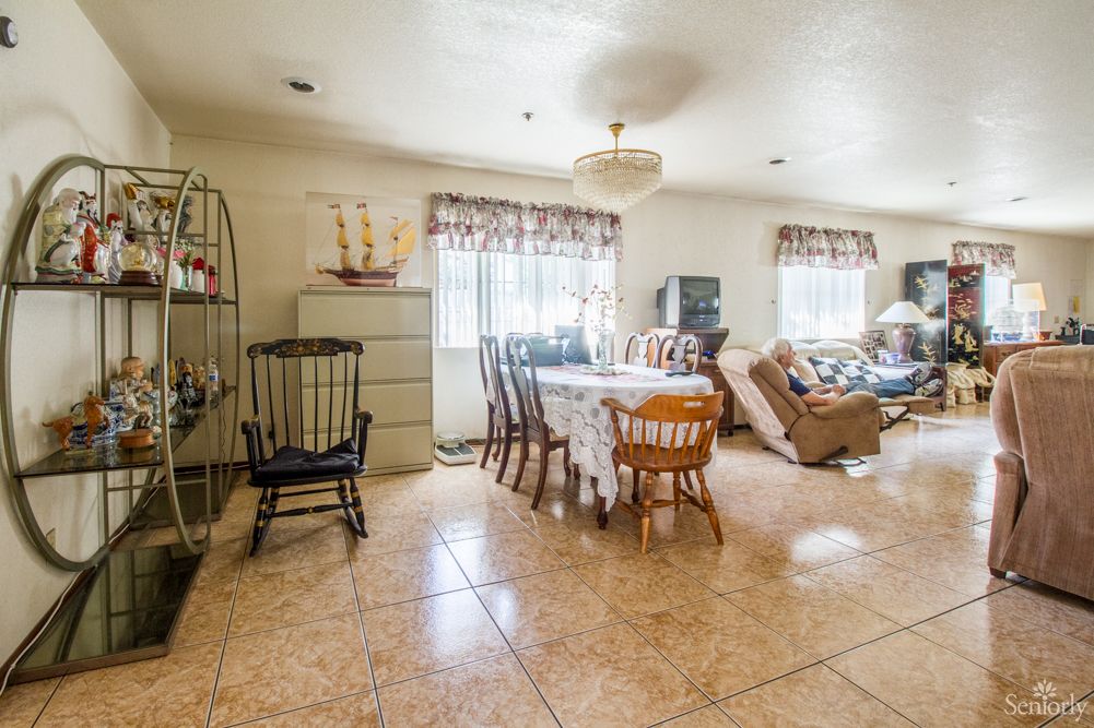 A cozy living and dining area with wooden furniture, large windows, and tiled flooring.
