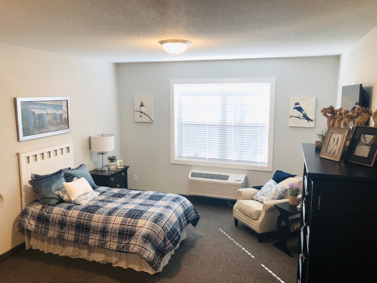 A cozy bedroom with a plaid bedspread, an armchair, and wall decor.