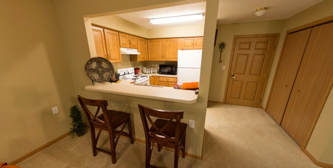 A cozy kitchen with wooden cabinets, a counter, and two chairs.