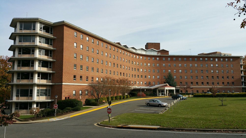 A brick hospital building with a parking area in front.