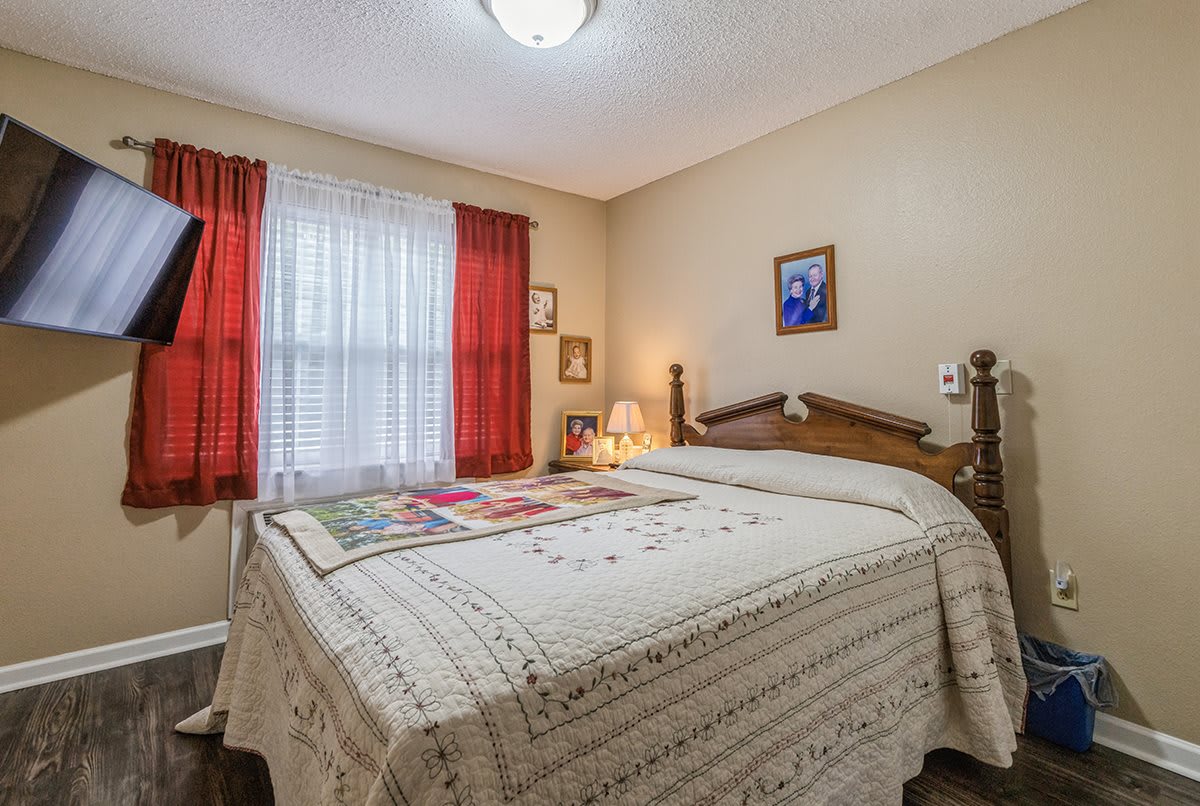 A cozy, traditional bedroom with a neatly made bed, red curtains, and warm lighting.