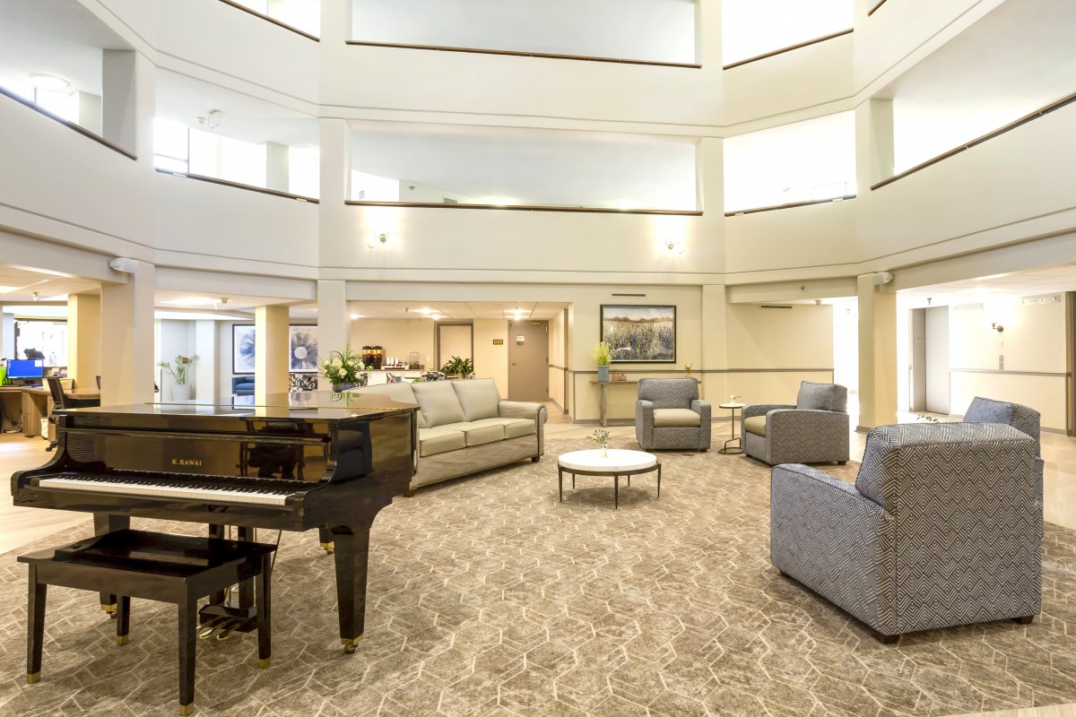 A spacious lobby with comfortable seating and a grand piano, featuring bright lighting and elegant decor.