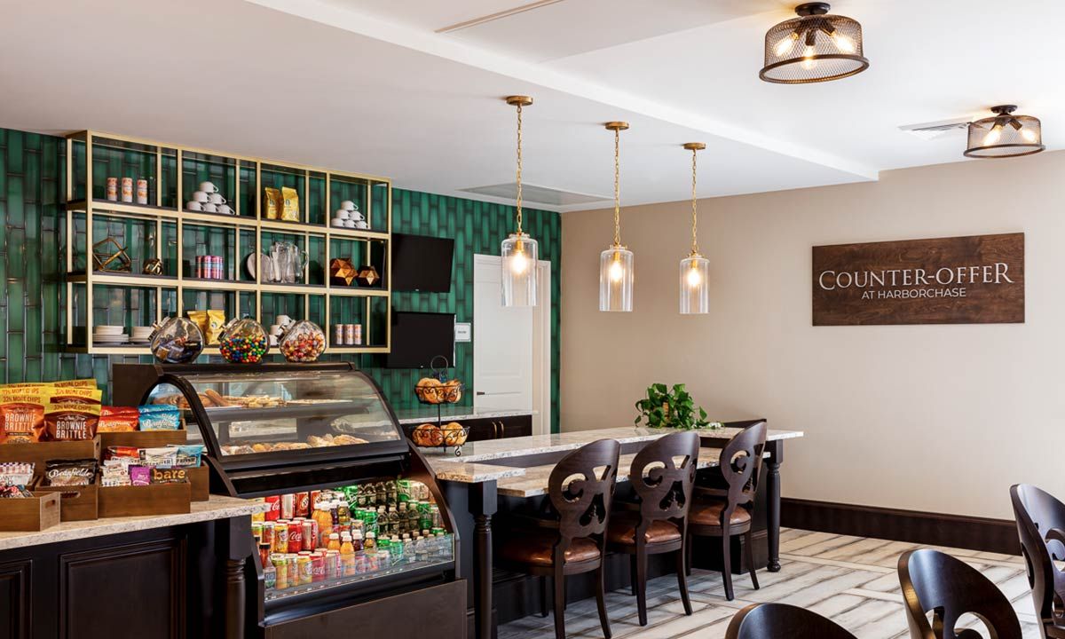 A cozy coffee shop interior with a modern design featuring pendant lights, a display case, and a green accent wall.
