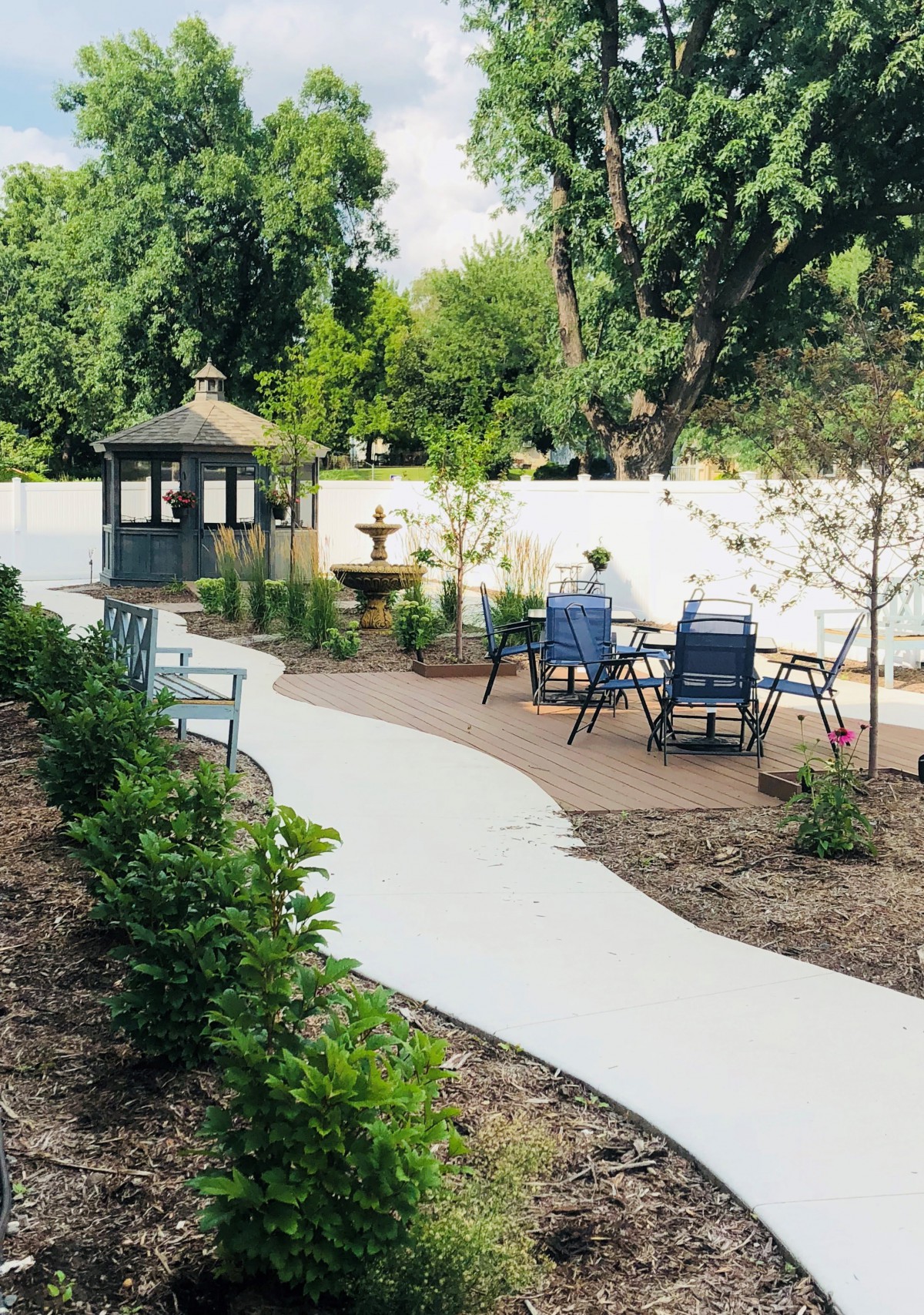 A beautifully landscaped garden with a winding pathway leading to a gazebo, featuring outdoor seating and a fountain surrounded by lush greenery.