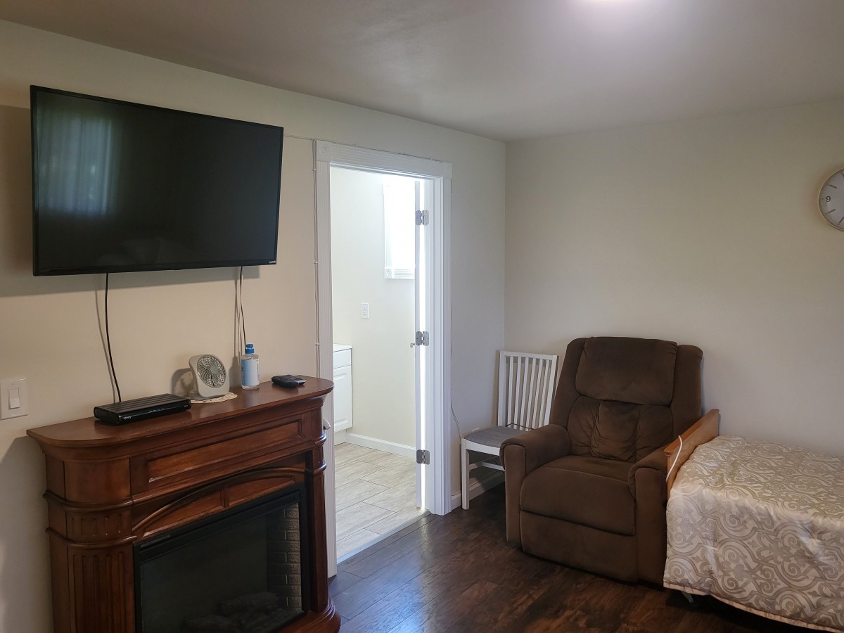 A cozy living room with a TV mounted above a fireplace, a recliner and chair near a doorway.