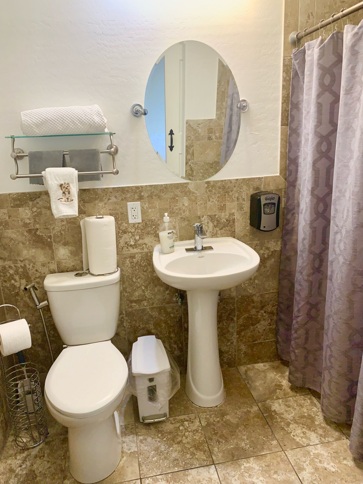 A small bathroom featuring a toilet, pedestal sink, and a circular mirror with neatly arranged toiletries.