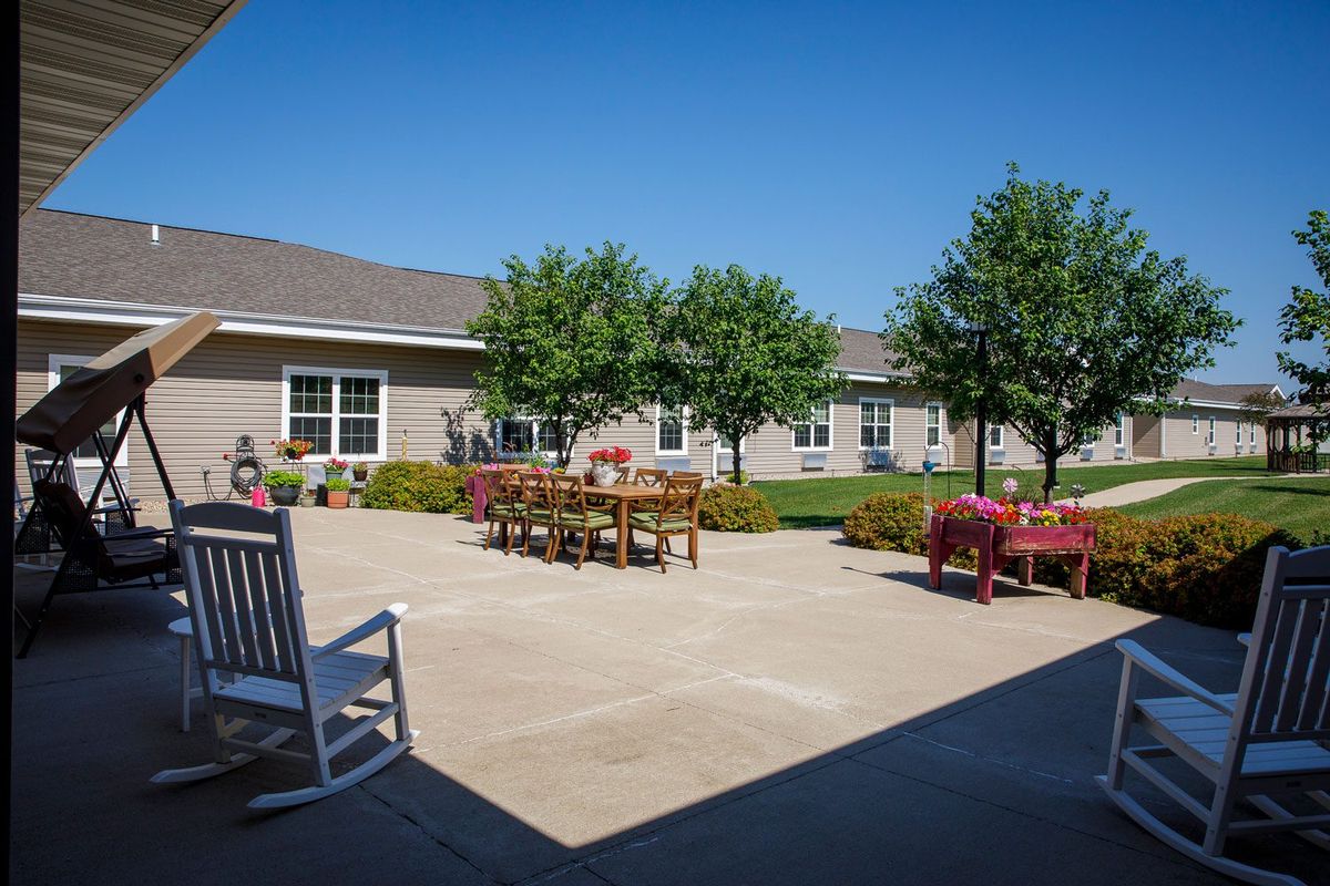 A sunny courtyard with outdoor seating, surrounded by trees and a building.