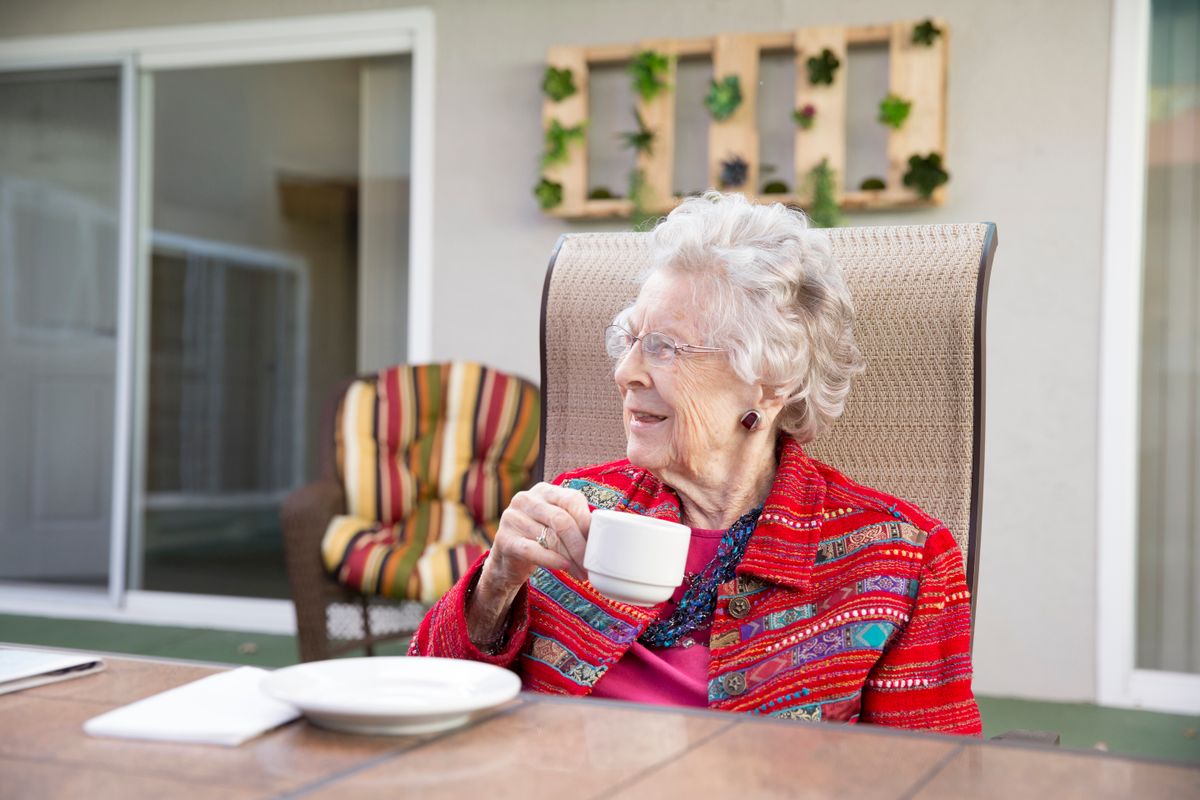 An elderly woman enjoying a cup of tea while sitting outdoors.