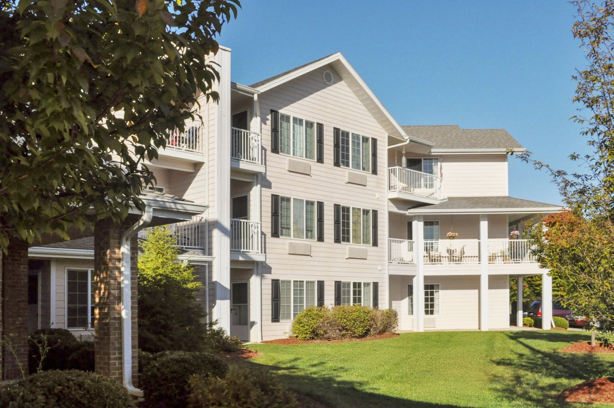 A modern apartment building with balconies and a well-maintained lawn on a sunny day.