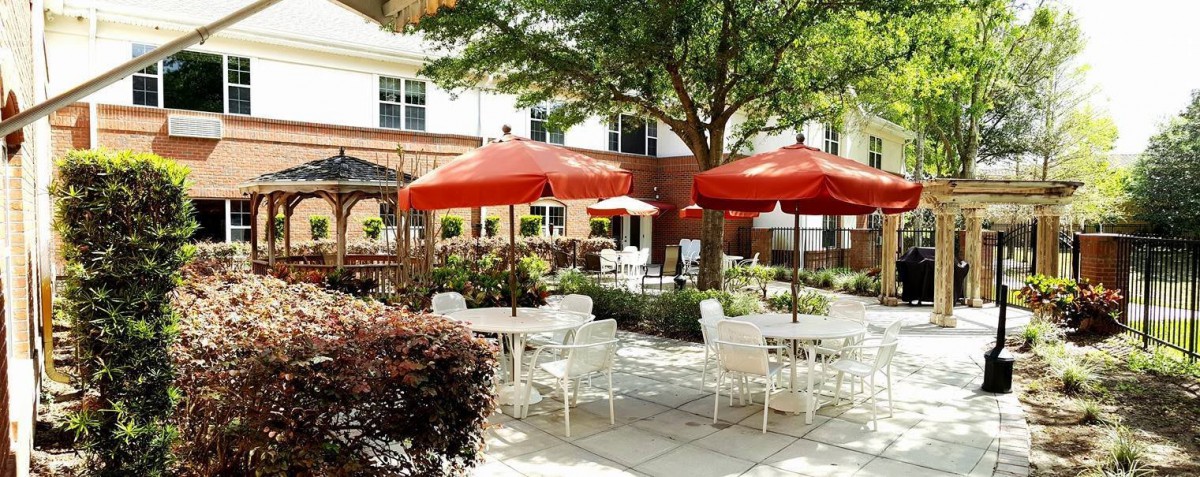 A charming outdoor patio with tables and chairs under bright red umbrellas, surrounded by lush greenery.