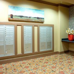 An interior view of a mailroom with multiple mailboxes, decorative flooring, and a painting on the wall.