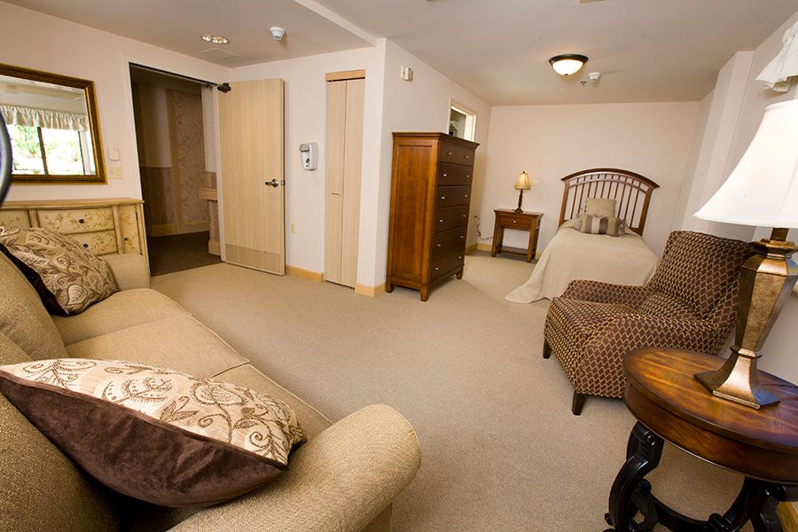 A cozy bedroom with a bed, dresser, and seating area.