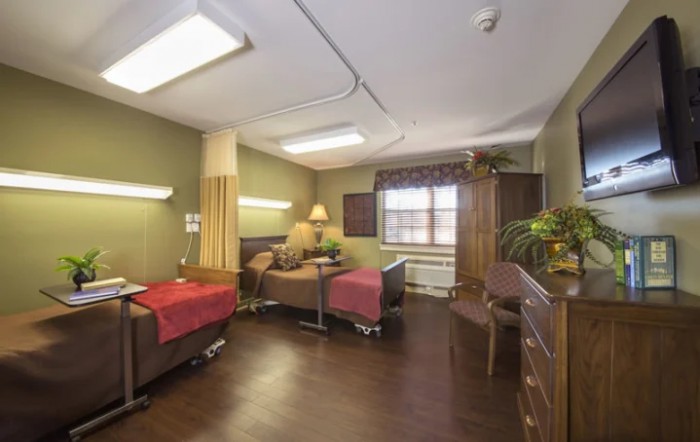 A hospital room featuring two beds, medical equipment, and warm lighting.