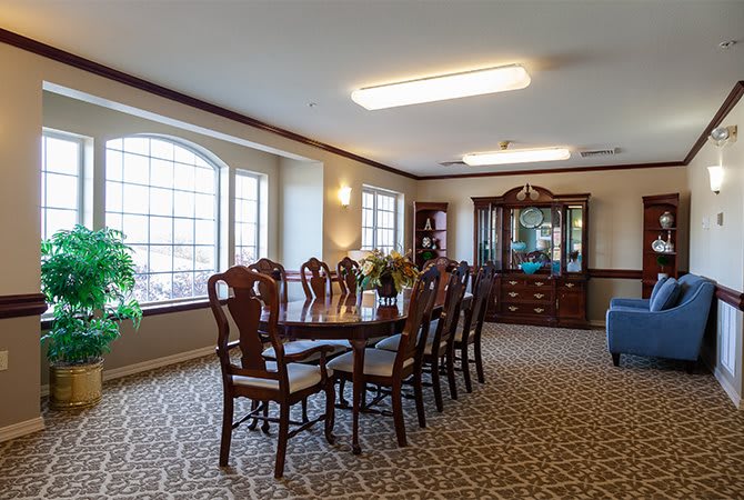 A classic dining room setup with a large table, chairs, and a display cabinet by a window.