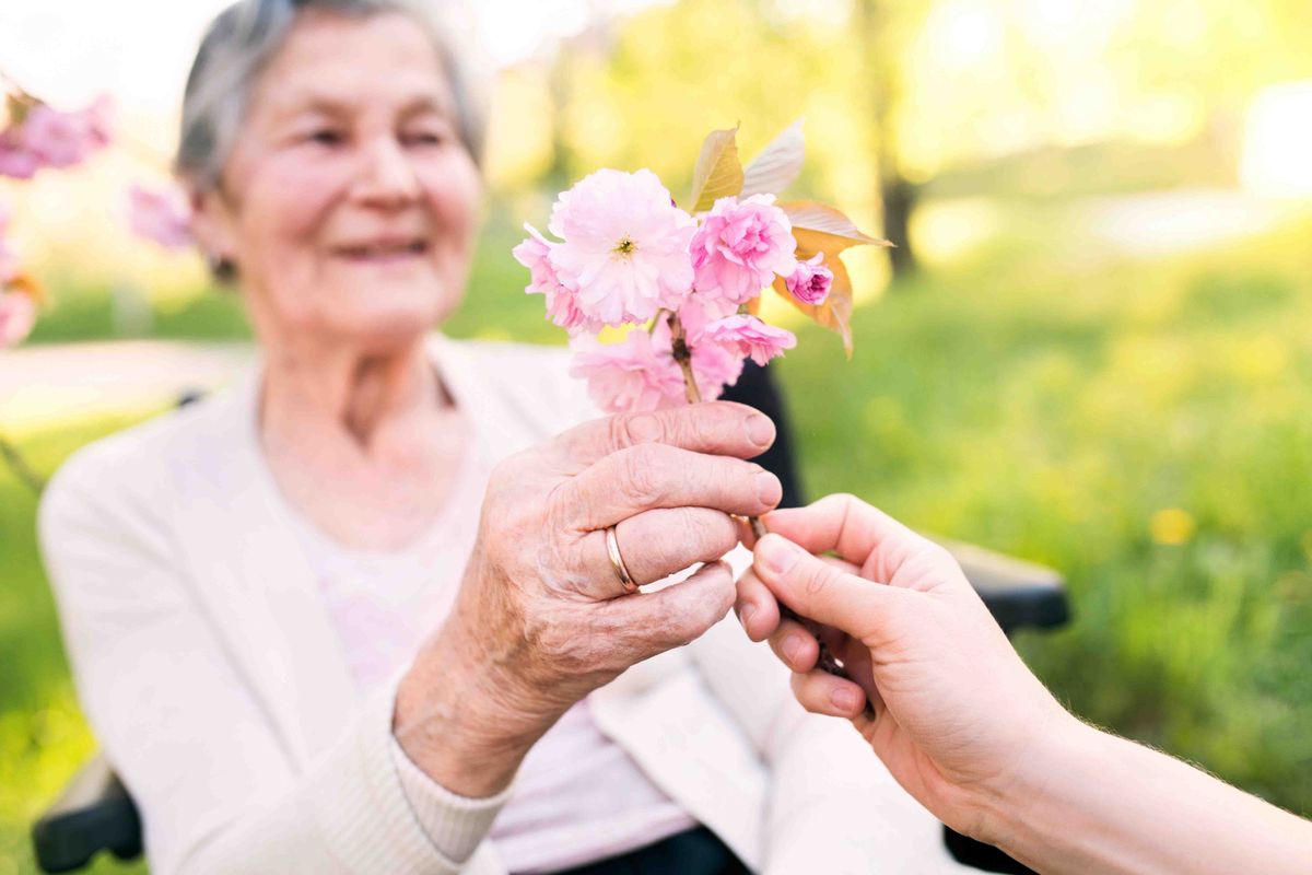 An elderly woman receiving a bouquet of pink flowers outdoors.