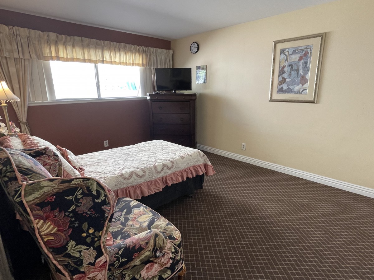 A cozy hotel room featuring a bed, armchair, and television with carpeted flooring.