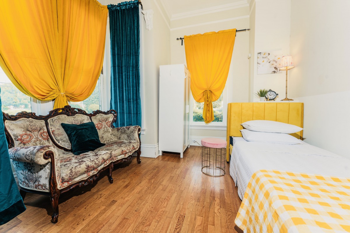 A vibrant bedroom featuring a mix of colorful curtains, a patterned sofa, and a bed with a checkered blanket.