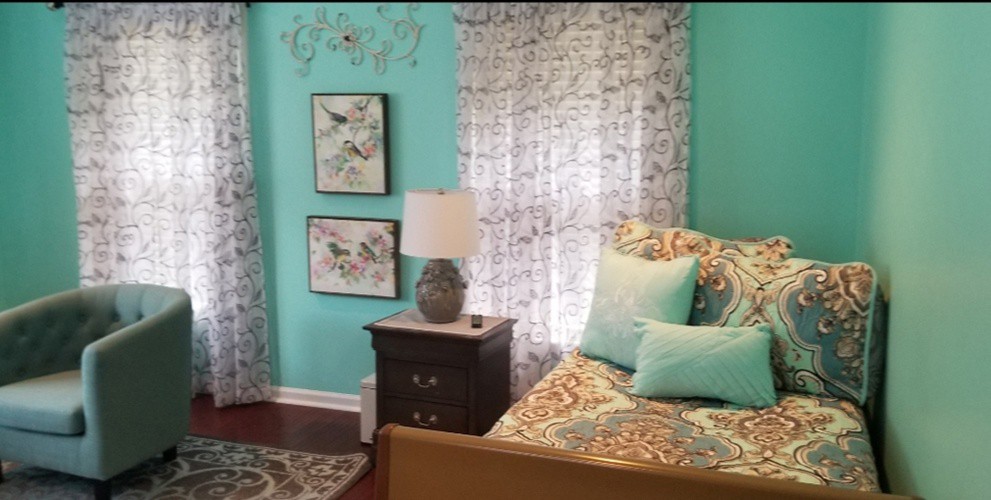 A cozy bedroom with turquoise walls, a bedside table with a lamp, and patterned cushions and curtains.